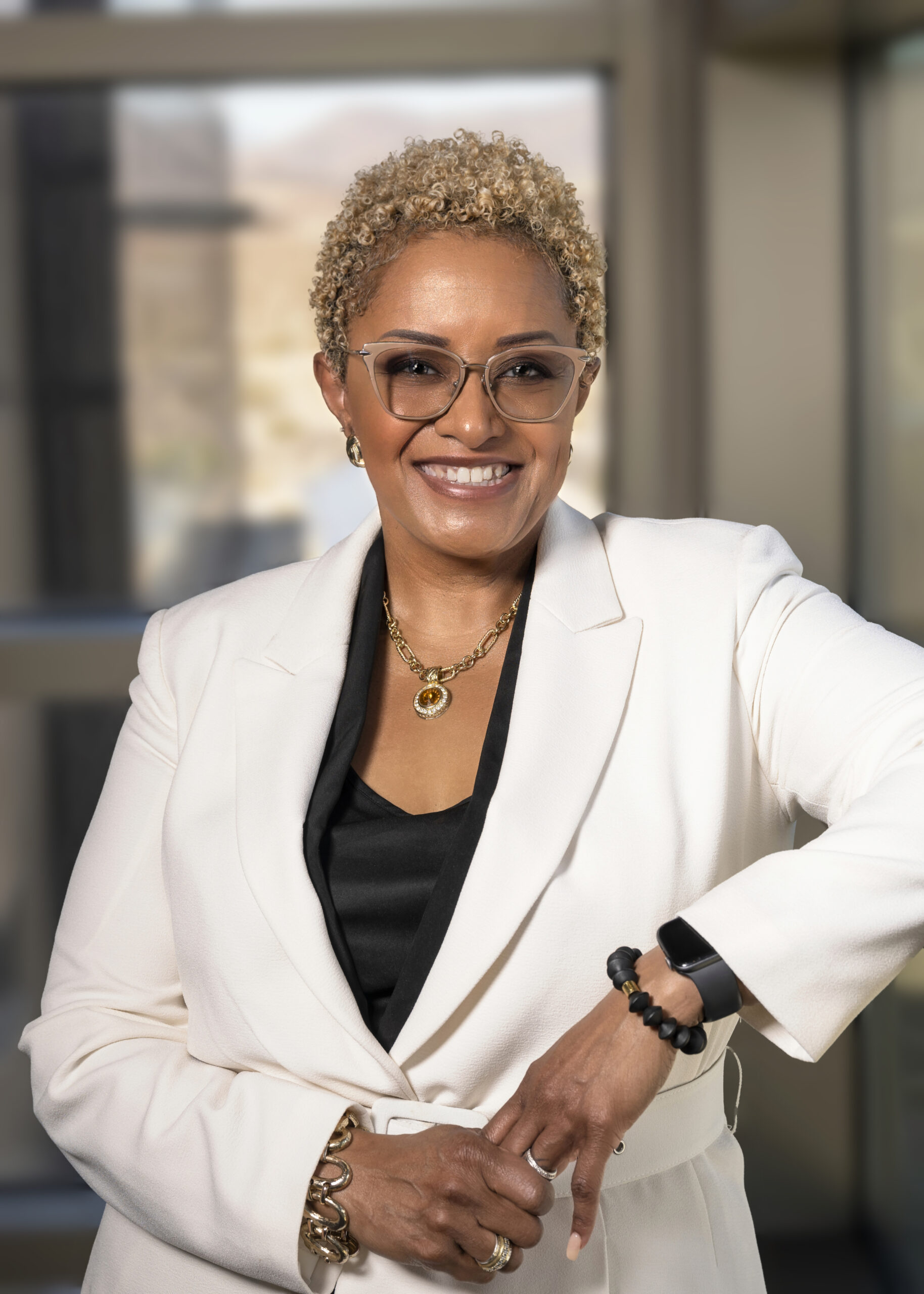 Professional woman in white blazer smiling, wearing glasses and gold jewelry