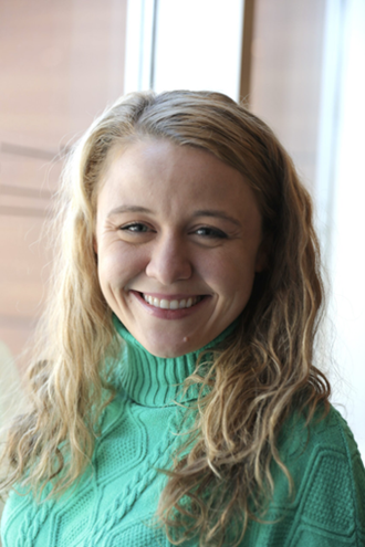 Smiling woman in teal cable-knit sweater standing near window