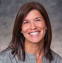 Professional woman in gray top smiling warmly against neutral background