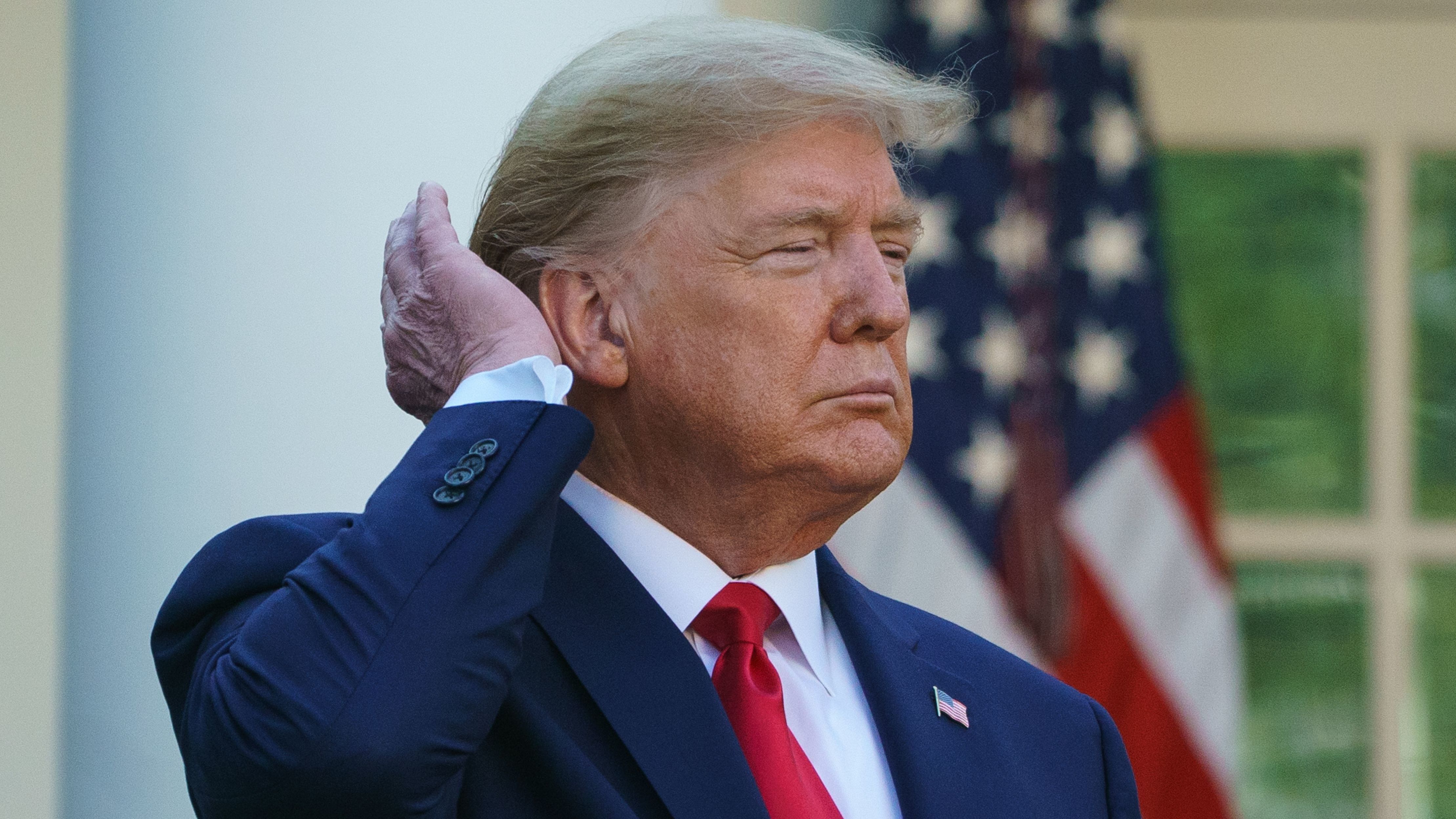Political figure in navy suit standing near American flag, looking serious