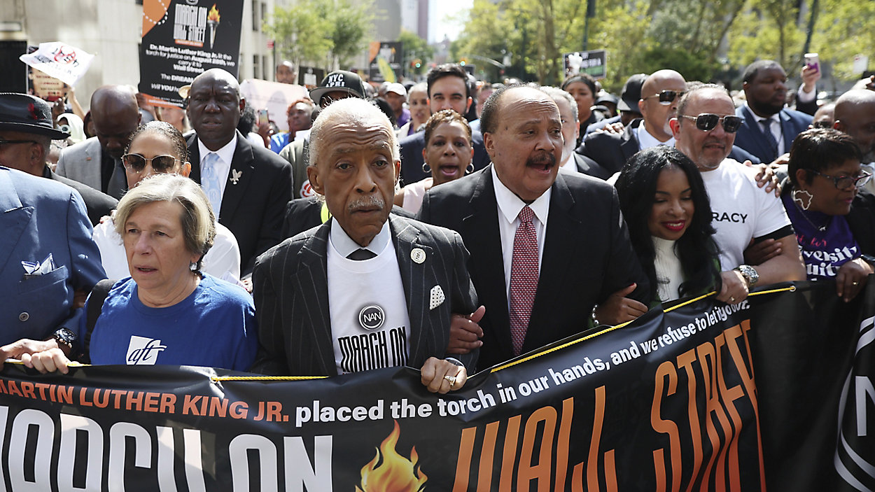 Civil rights leaders march together, holding banner about Martin Luther King Jr.'s legacy