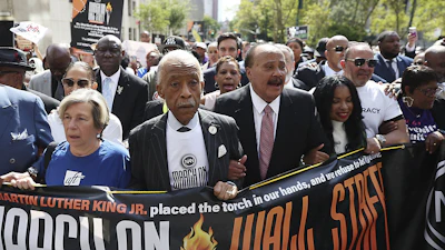 Civil rights leaders march together, holding banner about Martin Luther King Jr.'s legacy