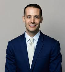 Professional man in navy suit and light tie against neutral background