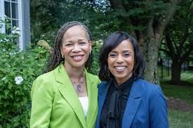 Two professional women smiling together outdoors, wearing green and blue blazers