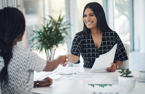 Smiling professional woman shaking hands across a white desk in an office