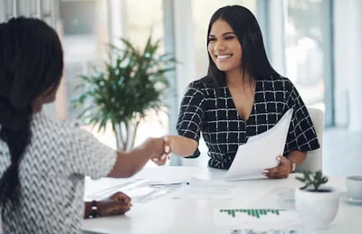 Smiling professional woman shaking hands across a white desk in an office