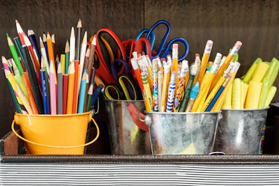 Colorful school supplies in metal and yellow buckets on striped surface
