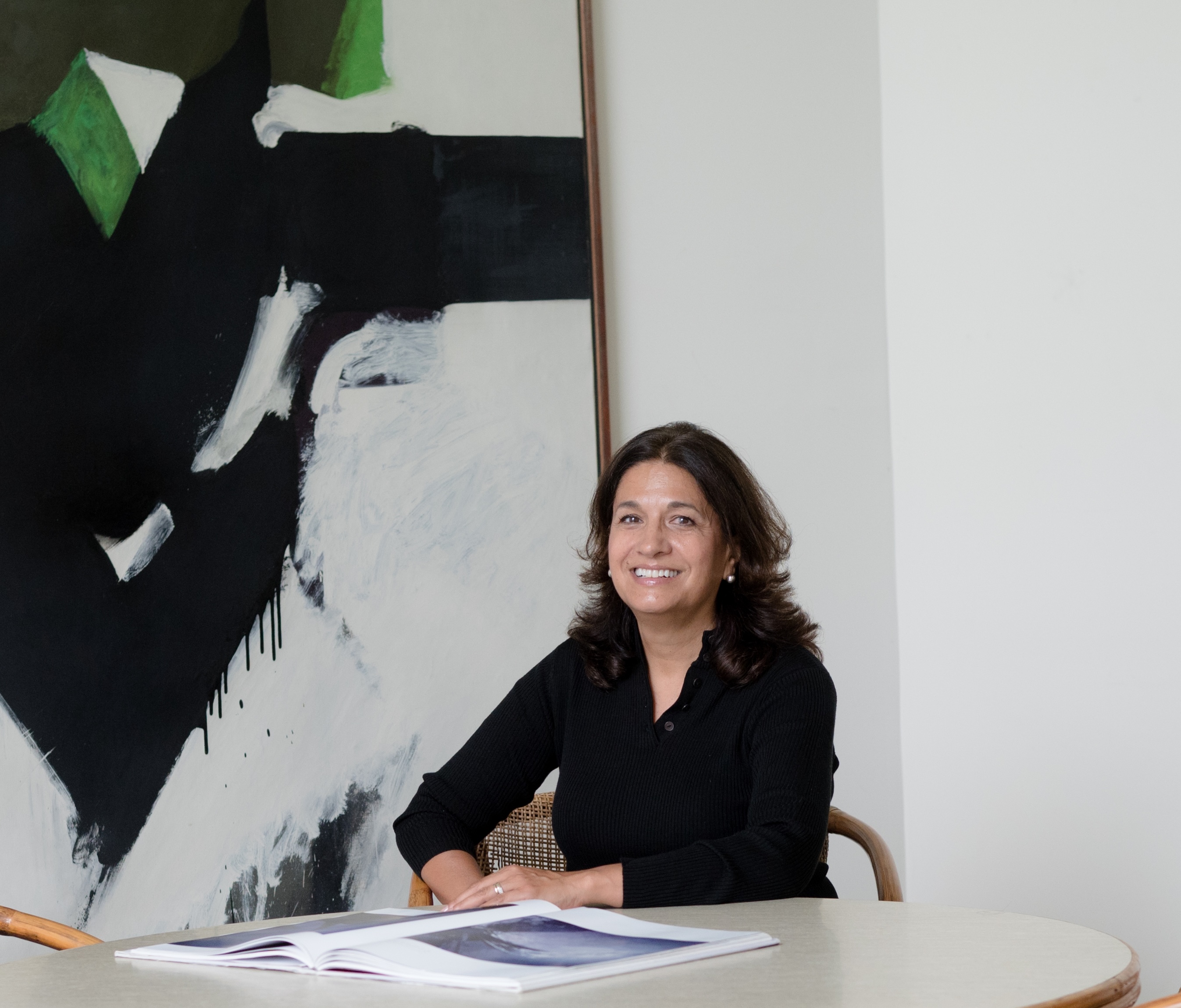 Professional wearing black shirt seated at desk with abstract black and white artwork on wall behind