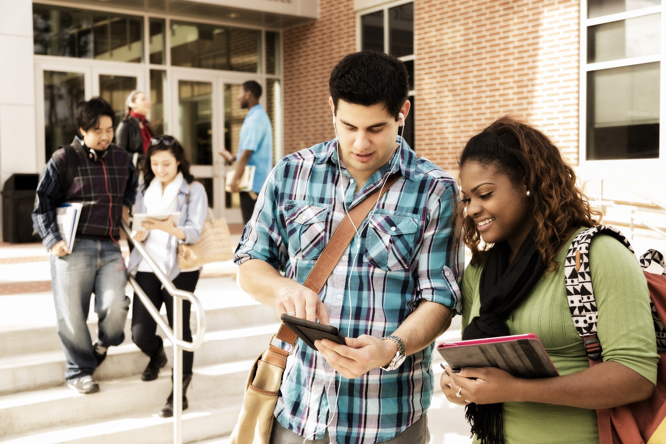 Students collaborating on campus, using tablets and textbooks near brick building