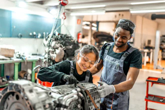 Two automotive technicians smiling while working on an engine in a workshop