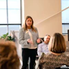 Professional woman presenting to colleagues in modern office with floor-to-ceiling windows and contemporary decor