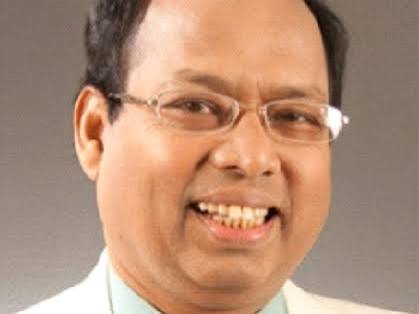 Professional headshot of a smiling man wearing glasses and a light blue shirt