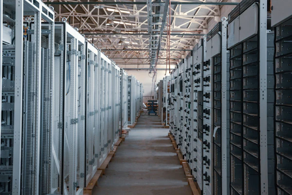 Industrial electrical substation with rows of white and black control cabinets and distribution panels in a warehouse facility