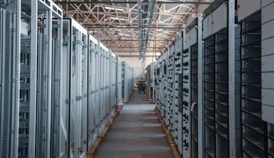 Industrial electrical substation with rows of white and black control cabinets and distribution panels in a warehouse facility