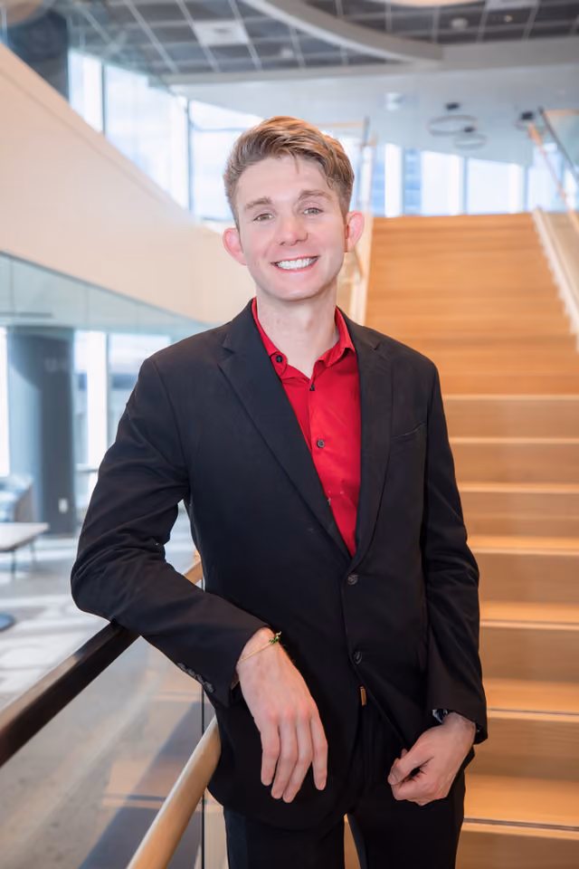Young professional man in black blazer and red shirt smiling in modern office stairwell