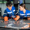Two technicians in blue uniforms assembling solar panels with orange tools in an industrial workshop