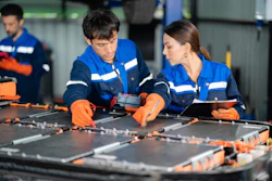Two technicians in blue uniforms assembling solar panels with orange tools in an industrial workshop